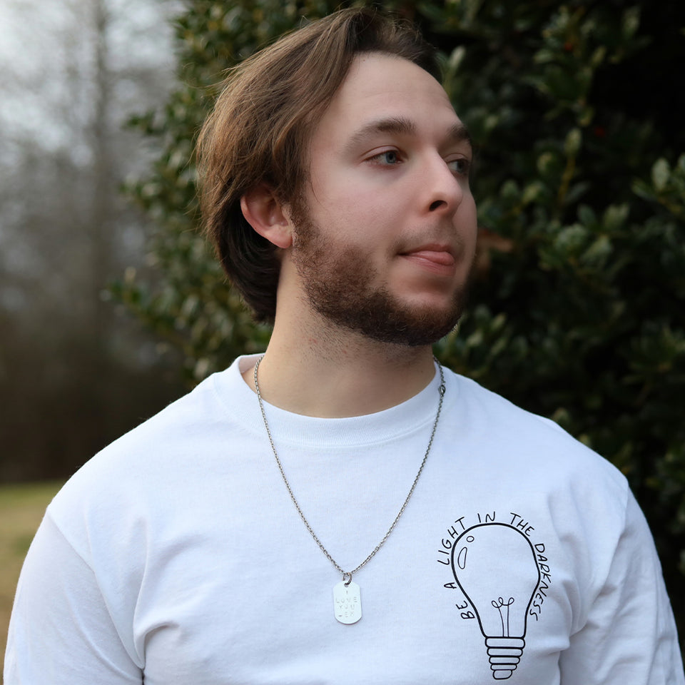 The Be A Light In The Darkness Long Sleeve T-Shirt in white being shown by a model looking off with the light bulb logo being the main focus to the right of the shirt. 